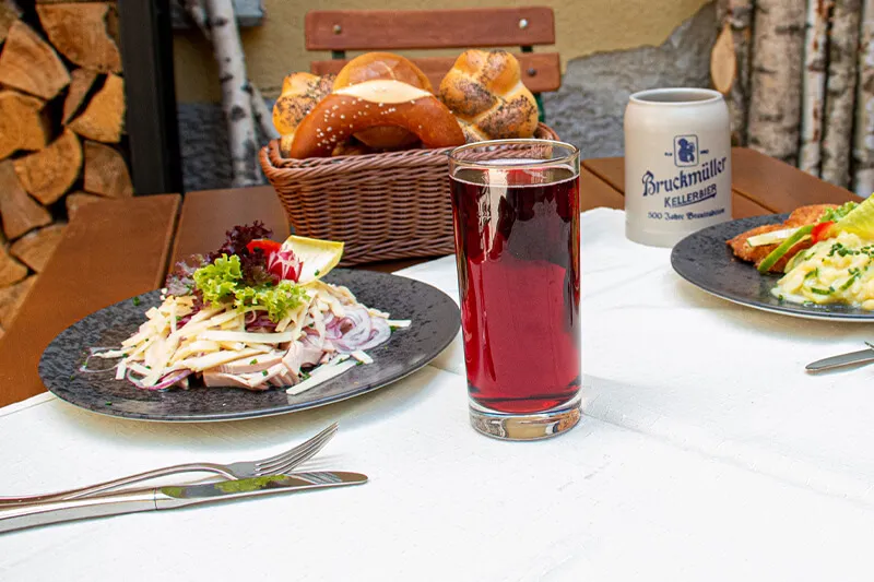 Mehrere Gerichte mit Getränken stehen auf einem Holztisch im Biergarten.