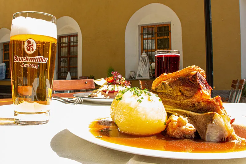 Ein Schweinebraten mit Knödel und einem Glas Bier stehen auf einem Tisch im Biergarten.