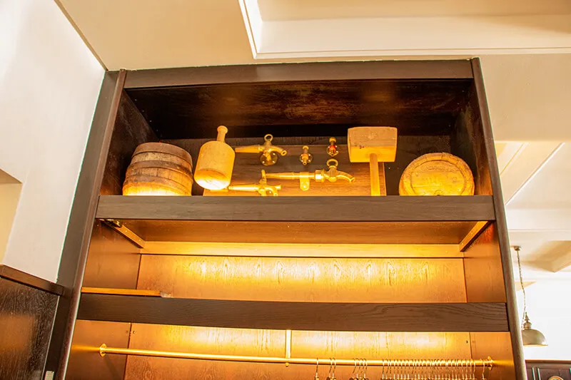 Historische Brauereiwerkzeuge aus Holz liegen in einem dunkelbraunen Schrank. 