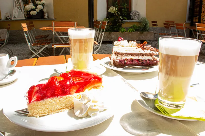 Mehrere Stück Kuchen mit Gläsern Latte Macchiato stehen auf einem Tisch.